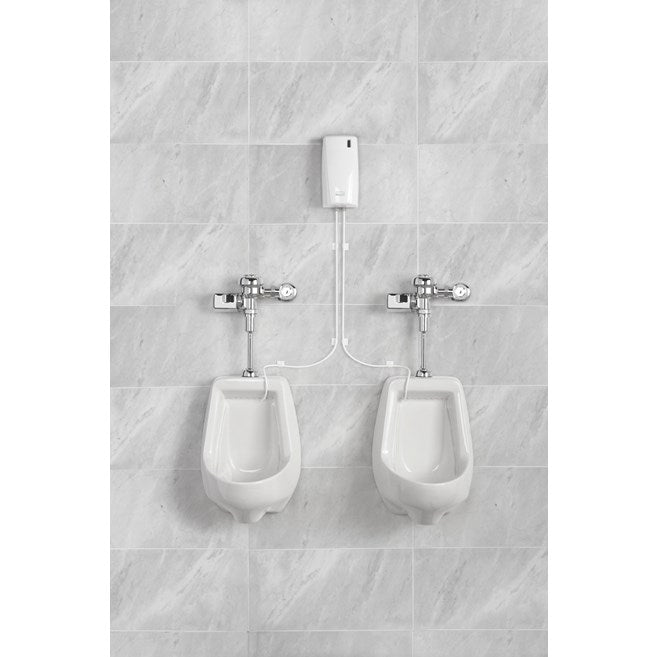 Doseador Ambientador Bacteriostático Urinol instalado acima de urinóis brancos em parede de azulejos cinzentos.