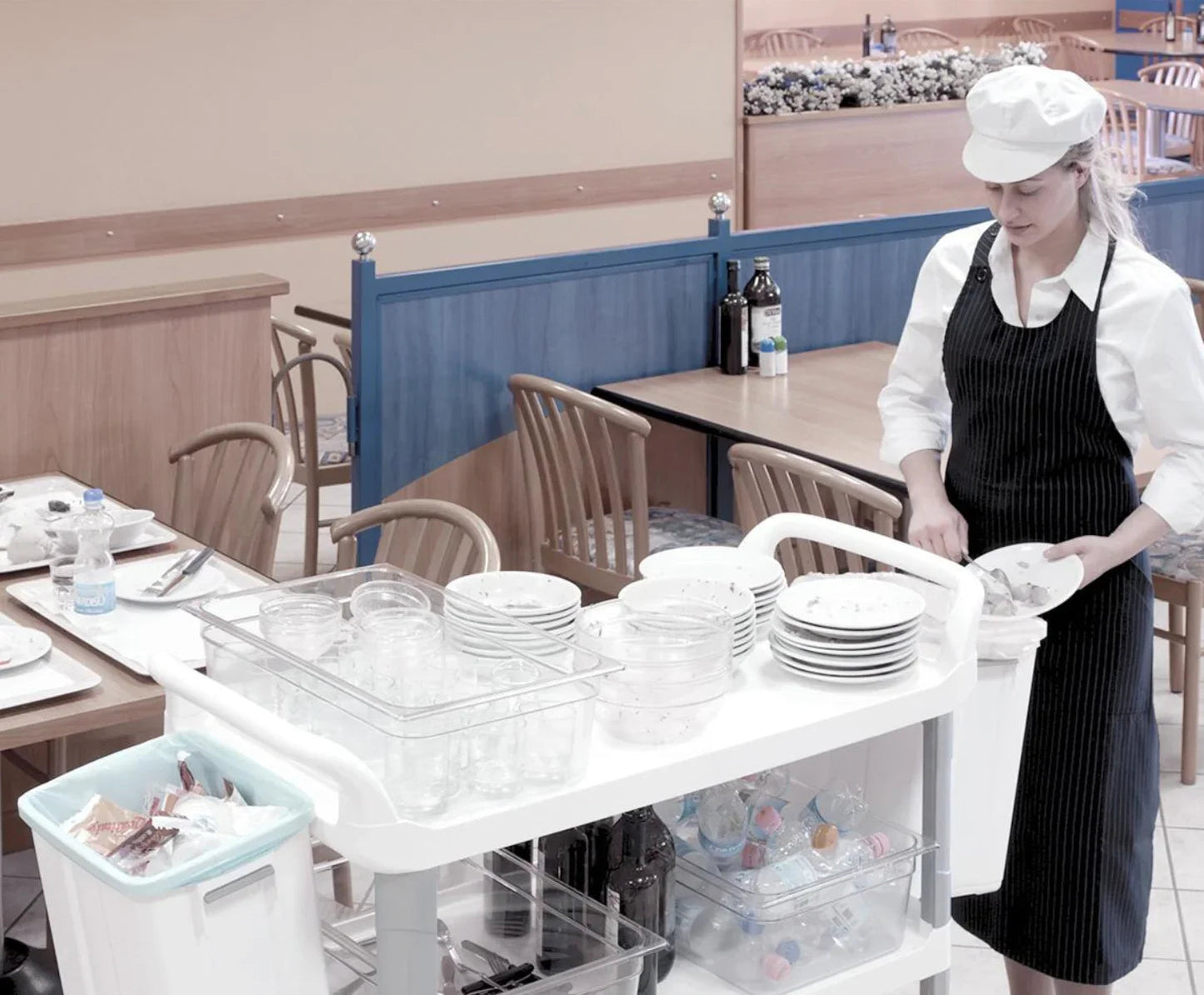 Funcionária de restaurante utilizando um carrinho de catering TTS para transportar pratos e utensílios.