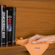 Pano do Pó Microfibras AntiEstático VILEDA laranja usado para limpar prateleira com livros ao fundo.