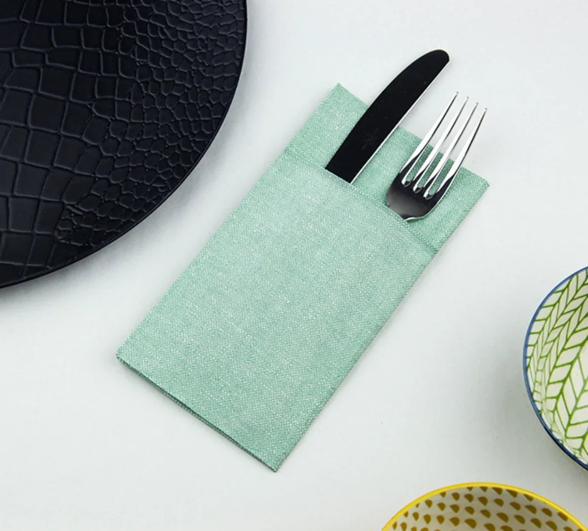 Guardanapos de Mesa Dobrados com Bolsa Kanguru Verdes com talheres preparados para uso.