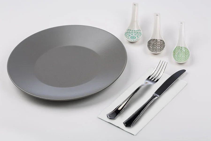 Mesa posta com um prato cinza, talheres prateados e colheres decoradas.
