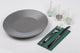 Guardanapos de Mesa Verdes Dobrados 1-8 PPP 40x40cm sobre prato cinza com talheres.