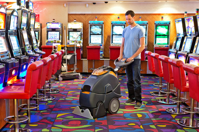 Lavadora Alcatifas Injeção e Extração Profissional TASKI em sala de jogos, limpando o tapete entre slot machines.