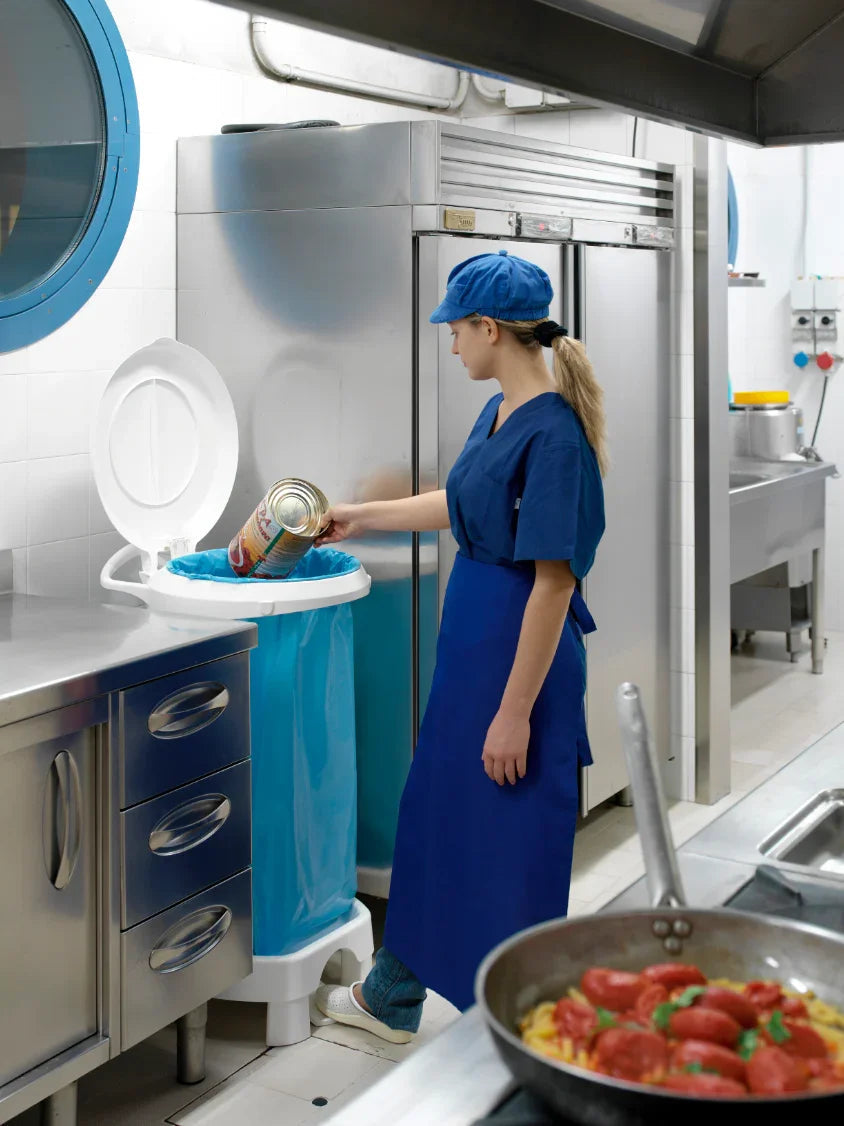 Funcionária a despejar lata em carrinho transporte para saco do lixo industrial na cozinha.