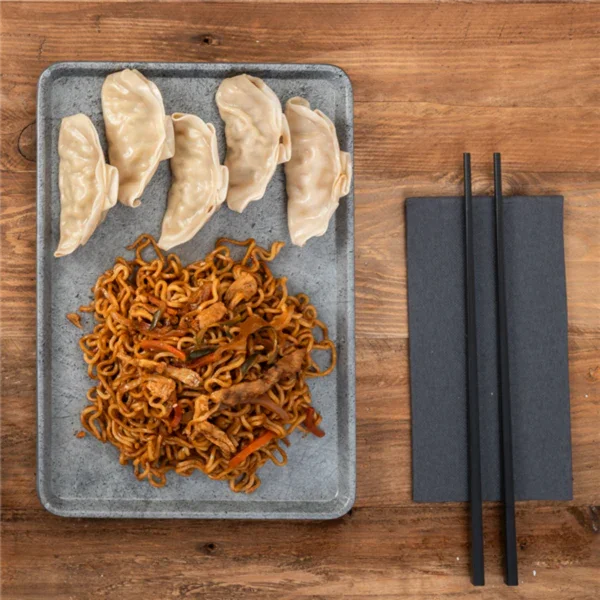 Prato com gyozas e noodles de carne, acompanhado de pauzinhos, sobre uma mesa de madeira