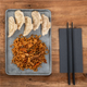 Prato com gyozas e noodles de carne, acompanhado de pauzinhos, sobre uma mesa de madeira